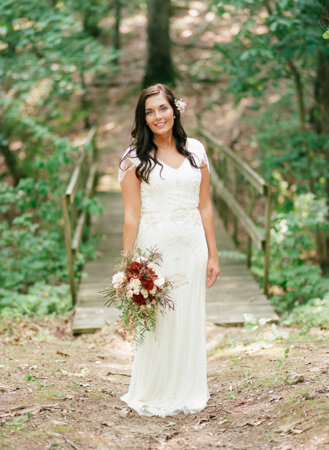 bride smiling in front of bridge in the woods, wearing beaded gown, Erica Robnett Photography