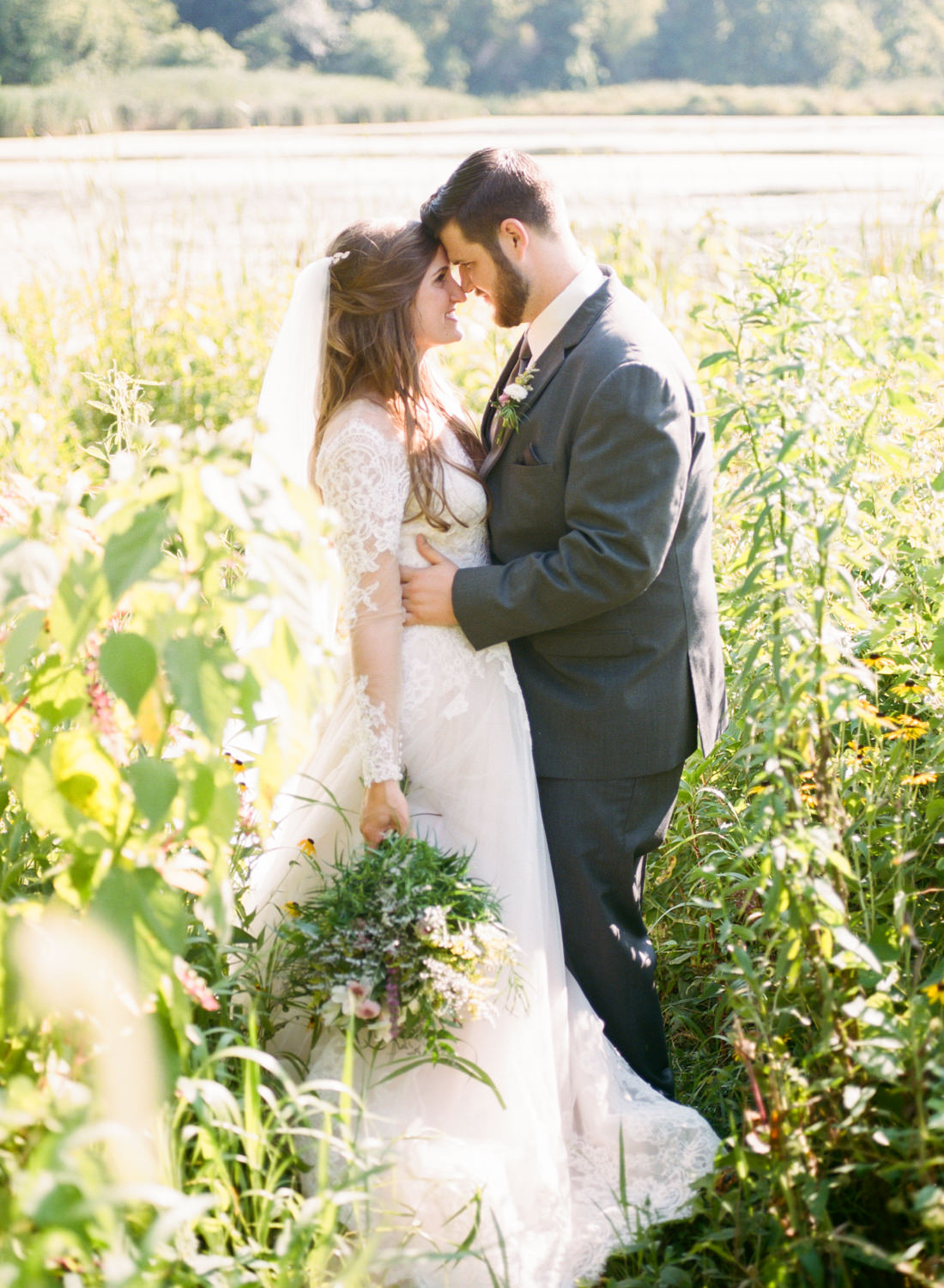 Bride and groom smiling in field with lake; St. Louis fine art film wedding photographer Erica Robnett Photography