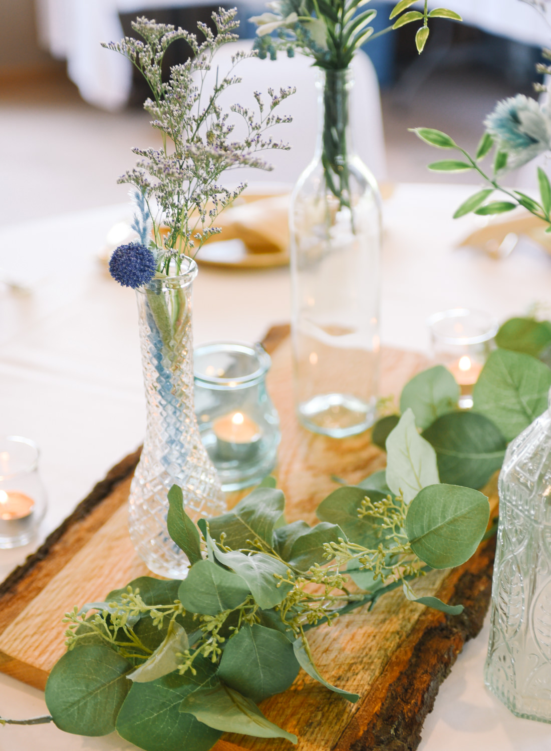 Vintage bottles, wood plank and greenery wedding reception decor; St. Louis wedding photographer