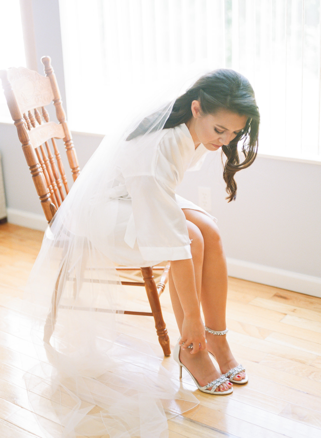 Bride putting on shoes by window; St. Louis film wedding photographer