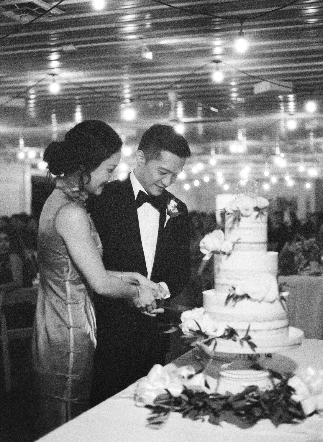 Grainy black and white film photo of bride and groom cutting cake at Defiance Ridge Vineyards