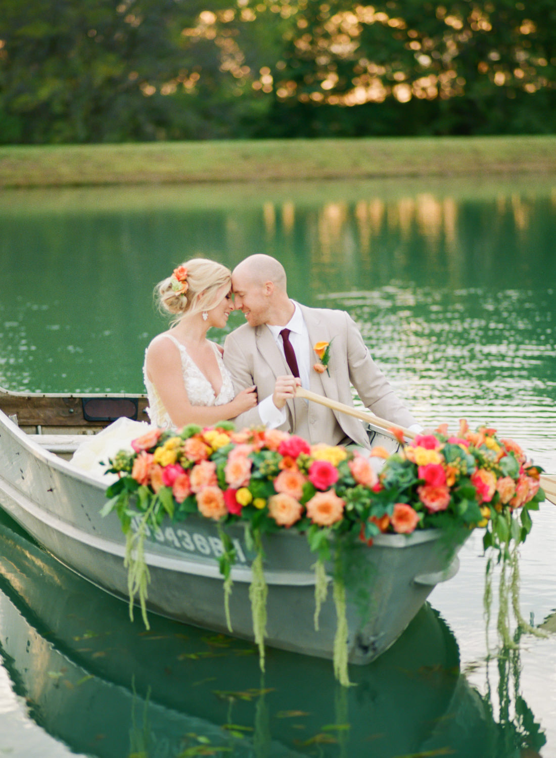 Bride and groom in a boat with brightly colored peach, orange, and yellow flowers at Missouri wedding venue Emerson Fields; St. Louis fine art film wedding photographer Erica Robnett Photography