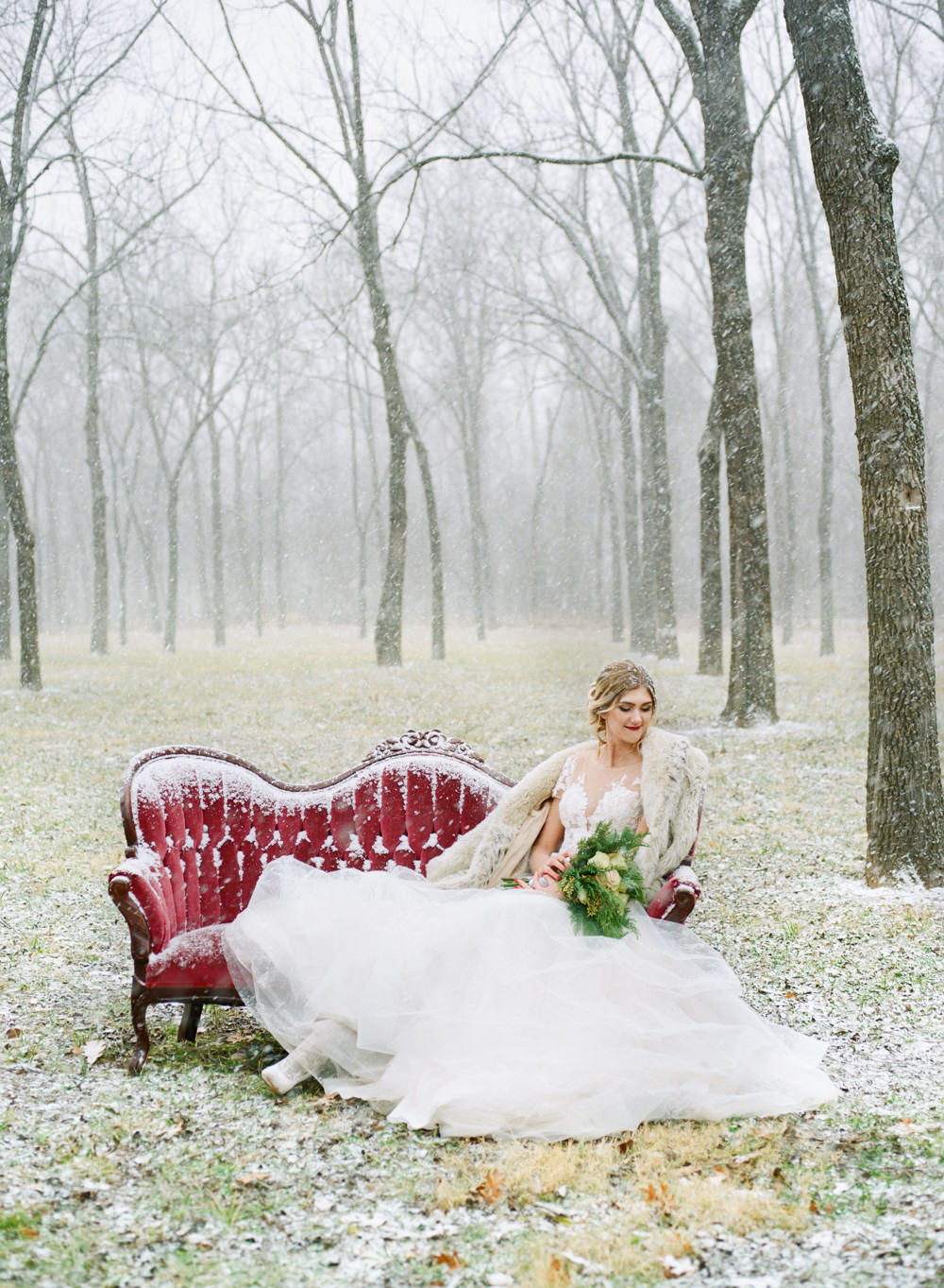 Winter wedding, bride with fur coat on red couch in snow; St. Louis fine art film wedding photographer Erica Robnett Photography