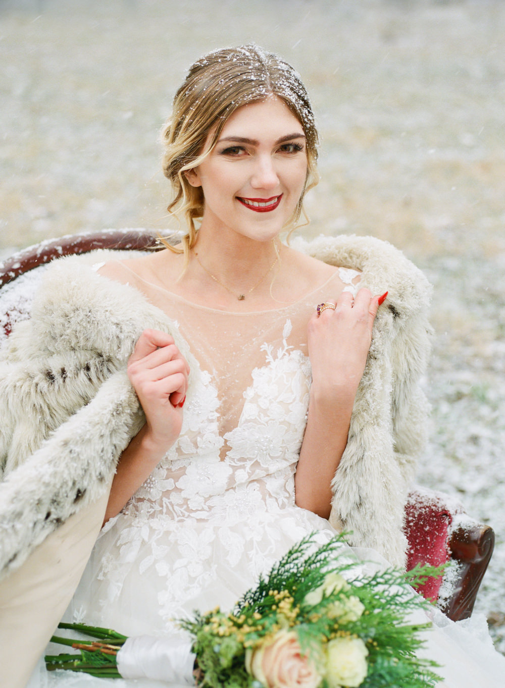 Winter wedding, Bride with fur coat on red couch in snow; St. Louis fine art film wedding photographer Erica Robnett Photography