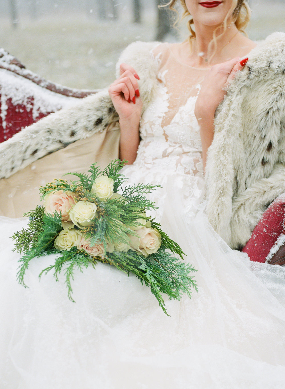 Winter wedding, Bride with fur coat on red couch in snow; St. Louis fine art film wedding photographer Erica Robnett Photography