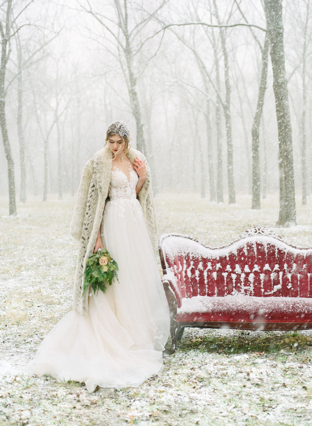 Winter wedding, Bride with fur coat and red couch in snow; St. Louis fine art film wedding photographer Erica Robnett Photography